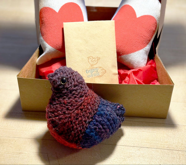 Knitted bird toy in front of a box with heart-shaped bags inside